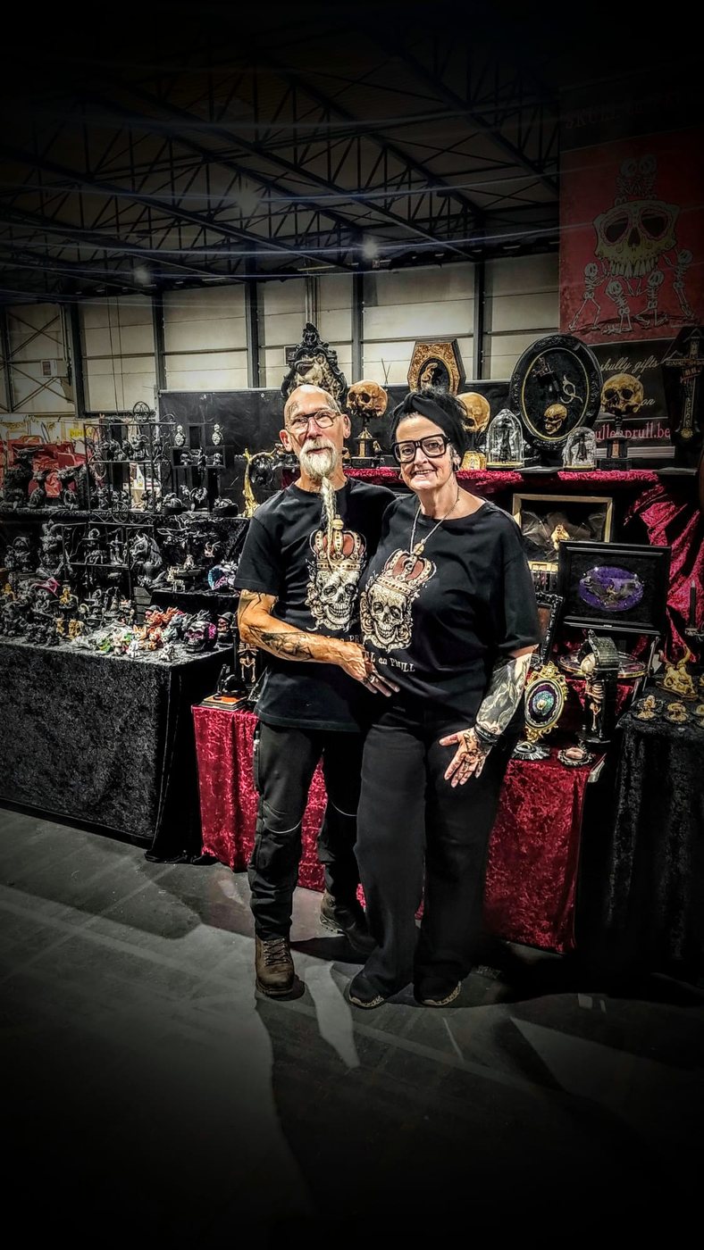 Elly and Flipke arm in arm in matching crowned skull shirts at their market stall.