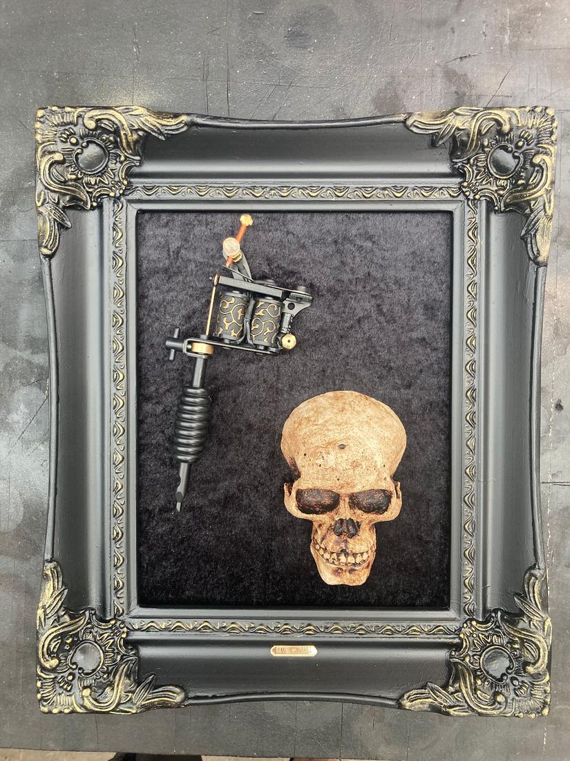 Gold skull and a real tattoo machine mounted together in a baroque frame.